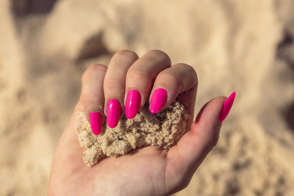 Hands with bright pink nails holding golden sand