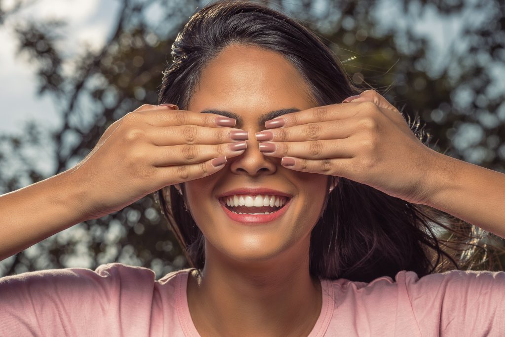 Smiling woman covering her eyes with pink manicured hands